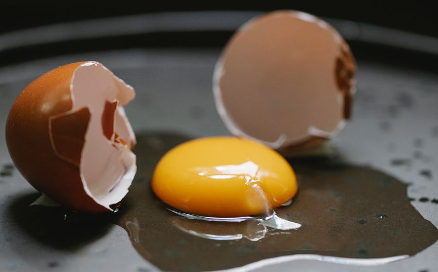 Un œuf fraîchement cassé dans une poêle noire, avec son jaune orangé bien rond et les deux moitiés de coquille brune posées de chaque côté